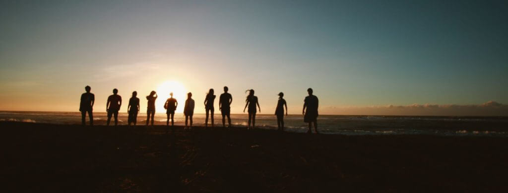 Community image of people on a hillside with sunset behind.